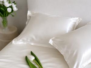 White mulberry silk pillowcases with pearl sheen on a minimalist bed, styled with white tulips in a calm bedroom setting
