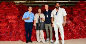 Waste2Wear and Kwality Holdings representatives standing in front of stacks of red recycled material at the Waste2Wear manufacturing facility