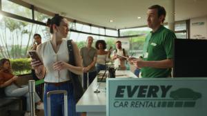 A girl at a rental car counter, holding a phone, looking at the attendant.