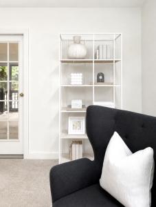 Modern staged reading nook featuring a black accent chair, decorative shelving, neutral accessories, and minimalist designer styling.