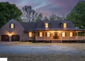 Twilight exterior of a luxury home in Richmond, Virginia featuring a wraparound front porch, illuminated windows, mature trees, and professionally presented curb appeal.
