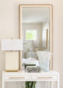 Designer-styled entryway console featuring a large mirror, modern table lamp, decorative accessories, and elegant neutral décor in a professionally staged home
