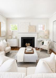 Professionally staged luxury living room with white seating, a classic fireplace, layered neutral décor, contemporary artwork, and abundant natural light.