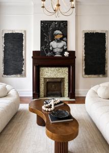 Professionally staged historic living room in Richmond, Virginia featuring a restored wood fireplace, sculptural boucle sofas, contemporary artwork, a modern wood coffee table, and luxury designer furnishings.