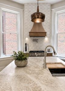 Luxury kitchen featuring a marble waterfall island, custom copper range hood, professional gas range, designer tile backsplash, and large historic windows.