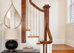 Historic home entryway with original curved wood staircase, designer table lamp, decorative mirror, and professionally styled console vignette.