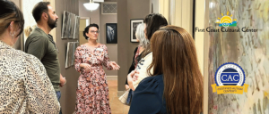 A woman in a floral dress explains art to a group inside a gallery at First Coast Cultural Center, certified autism center.