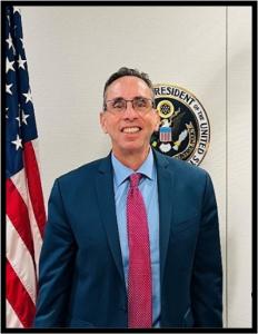 Richard J. Baum, former Acting Director of ONDCP, standing beside the White House Office of National Drug Control Policy seal.