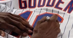 Dwight "Doc" Gooden's hands signing the number 16 on a white Mets pinstripe jersey