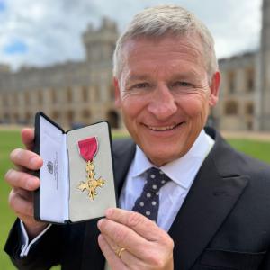 Close-up portrait of Jeremy Kelly holding an open presentation box containing his OBE insignia following his June 2026 investiture at Windsor Castle.