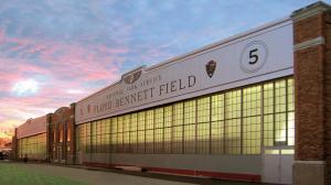 Exterior view of the historic Hangar 5 at Floyd Bennett Field in Brooklyn, New York, during sunset. The restored hangar features large industrial glass windows, brick architecture, and prominent "Floyd Bennett Field" signage with National Park Service bra