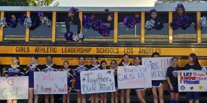  A group of smiling students hold up signs while standing in front of a GALS LA school bus.