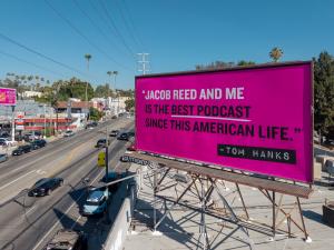 A pink billboard with white and black text reads "Jacob Reed and Me is the best podcast since This American Life — Tom Hanks"