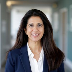 Headshot of Veena Vadgama smiling, wearing a navy blazer over a white shirt.