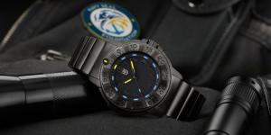 Luminox Navy SEAL Foundation XS.3228.NSF watch with illuminated Luminox Light Technology (LLT), displayed on tactical gear alongside flashlights and a Navy SEAL Foundation patch.