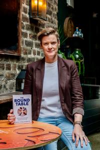 Author Sarah Stone McDevitt is sat holding her book The Round Table