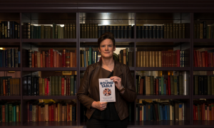 Author Sarah Stone McDevitt is stood in front of a bookcase of books with her book The Round Table