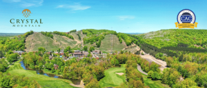 Aerial view of Crystal Mountain resort with green hills, golf course, and trees under a clear blue sky.