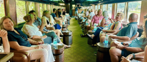 Passengers seated inside a vintage train car with large windows, engaging in conversation and enjoying bottled water.