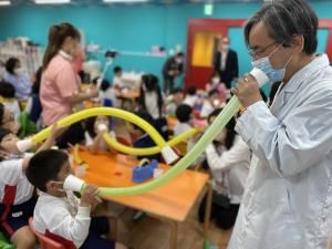Preschoolers use long tubes to explore how sound travels while a specialist in a lab coat guides them