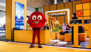 Upgames exhibition stand at ICE Barcelona 2026 featuring the company's red mascot, branded booth, interactive gaming stations, and visitors exploring its portfolio of mini games.