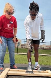 Ji'Ayir Brown, wearing sunglasses and heat-resistant gloves, uses a branding iron on a wooden bed frame as Sarah Fulton, in a red NJ-Morris Co. SHP shirt, watches beside him.