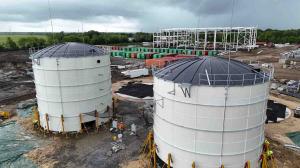 Water storage tanks under construction at LAMP in Liberty County, Texas, with workers and a steel manufacturing structure in the background.