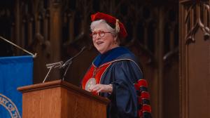 Photo of person wearing academic robes speaking at a podium in a church
