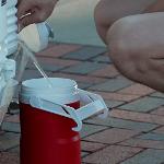 Photo of a man squatting down to fill up a red water jug with water coming out of a white water cooler.