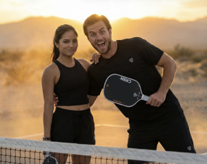 A happy couple holding CRBN paddles on the pickleball court at sunset