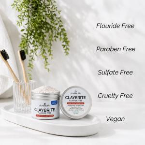 Zion Health CLAYBRITE® Tooth Powder displayed in a bright bathroom setting with bamboo toothbrushes and fluoride-free, paraben-free, sulfate-free, cruelty-free, and vegan claims.