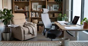 Ergonomic office chair and adjustable standing desk in a modern home office with a beige recliner sofa