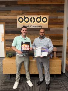 Obodo Energy Partners CEO John and partner Chris holding the Top Solar Contractors List magazine and smiling in front of the Obodo Energy Partners sign.