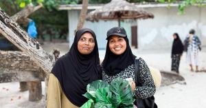 Two South Asian women wearing headscarves, standing outside in the daytime, one is smiling, looking to camera