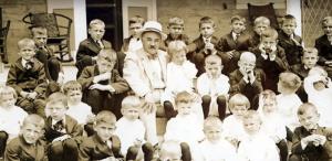 Milton Hershey is shown surrounded by a large group of children smiling.