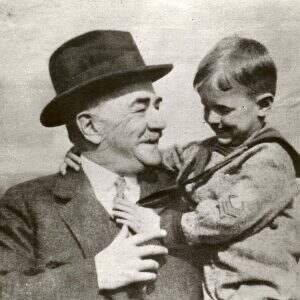 Milton Hershey is smiling, shown with a small child who is smiling at him.