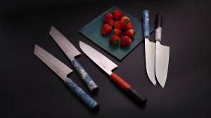 Japanese kitchen knives displayed with strawberries on a dark tabletop.
