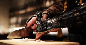 Close-up of a Japanese kitchen knife cutting vegetables, held by a person wearing samurai armor.