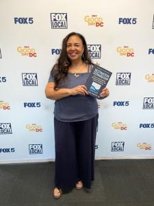 Author Tonya Fitzpatrick holding her book Destination Stewardship in front of a Fox 5 DC backdrop.