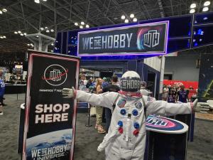 A person in an astronaut uniform in front of a trade show booth for We the Hobby