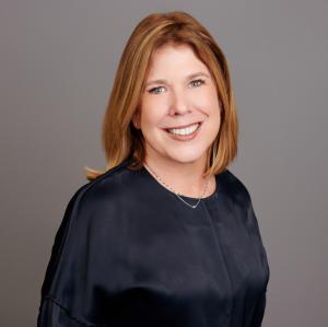 Photo of a woman with reddish brown hair smiling in a black shirt.