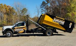 Buster's Dumpsters truck dropping a roll-off dumpster at its new yard for dumpster rental deliveries near Lansing MI