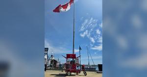 Red Coffee Bike beneath a large Canadian flag on the Halifax waterfront during THE CROSSING journey.