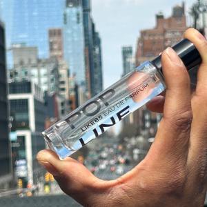 Hand holding LIKE85 POP LINE 15ml fragrance against the New York City skyline, highlighting the brand’s premium travel-size fragrance format