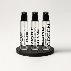 Three LIKE85 15ml fragrance bottles—POP LINE, RISKY BLUE, and BLIND GREEN—displayed on a branded stand representing the company’s premium travel-size fragrance collection.