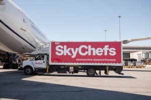 A SkyChefs airline catering truck sits next to an aircraft on the tarmac.