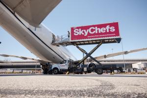 A SkyChefs airline catering truck is elevated next to an aircraft for catering.