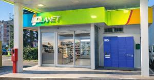 Exterior of an iPlanet convenience store at a fuel station, with glass doors, refrigerated displays and a blue GLS parcel locker outside.
