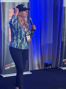 Sandy Wardenburg Waggett speaking on stage with a microphone at the Seven Figure Agency Intensive in Miami