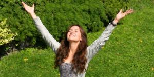 A young woman with eyes closed and arms outstretched, basking in a sun-drenched park.